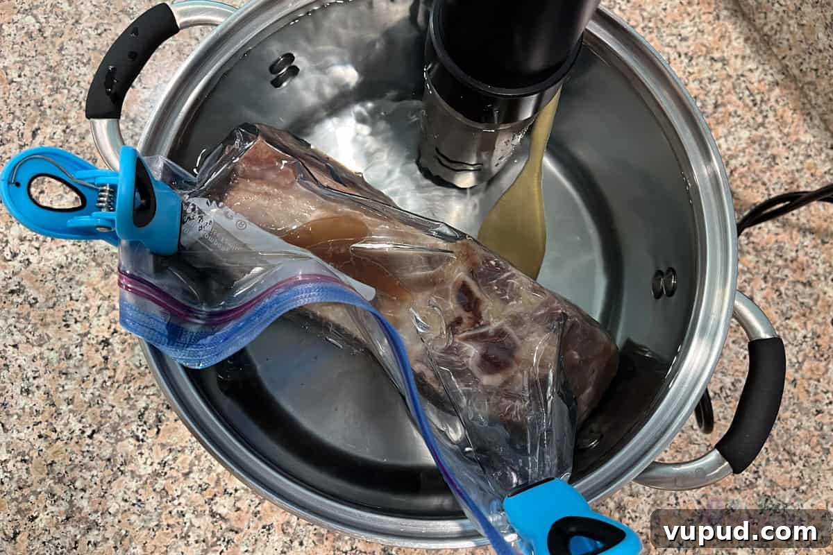 Perfectly Tender Sous Vide Prime Rib Roast Recipe 6 Rib roast cooking in a sous vide water bath, clipped to the side and with a wooden spoon at the bottom to keep from moving towards the circulator.