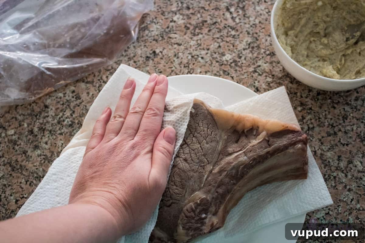 Perfectly Tender Sous Vide Prime Rib Roast Recipe 8 A hand patting the cooked but not seared roast dry with paper towels, while the compound butter sits to the right ready to use.