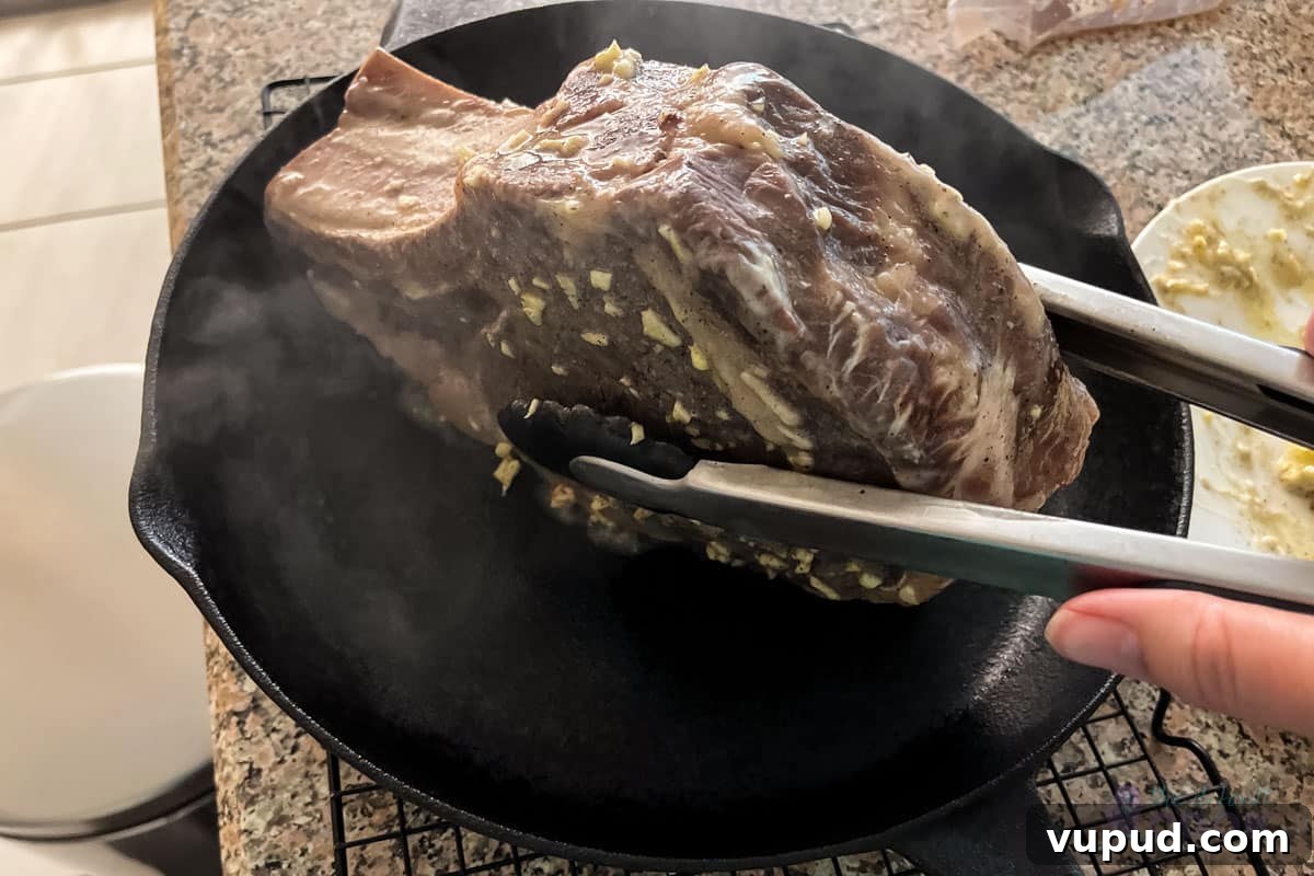 Perfectly Tender Sous Vide Prime Rib Roast Recipe 9 Tongs being used to carefully place a rib roast in the standing position into a hot cast iron skillet.