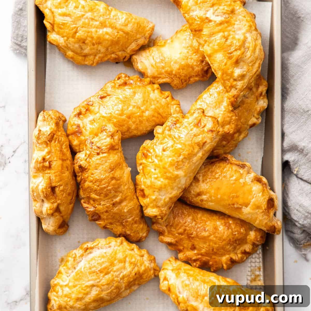 Tray of baked pasties, sitting on a grey cloth.