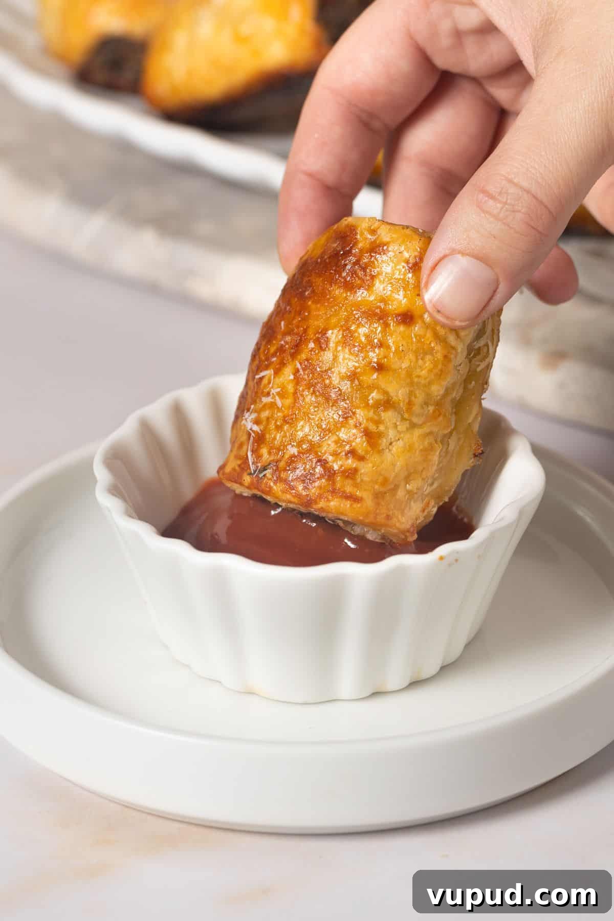 Mediterranean Beef Sausage Rolls with Herbed Feta and Spinach 10 Hand dipping a sausage roll into a small bowl of tomato ketchup.
