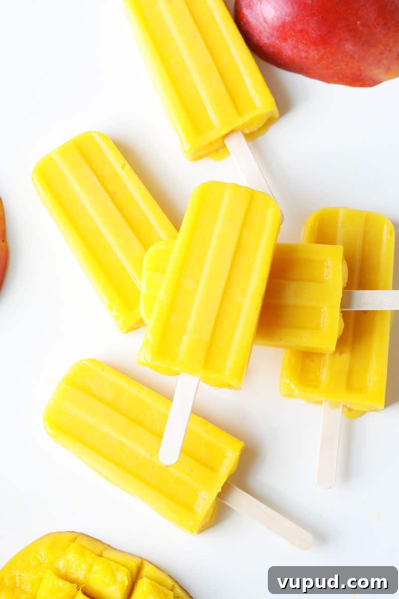 Mango Popsicle Recipe: Creamy, Refreshing Homemade Treat 2 a pile of mango popsicles on a white tray with a sliced fresh mango behind them