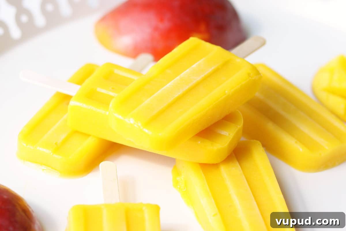 Mango Popsicle Recipe: Creamy, Refreshing Homemade Treat 6 a pile of mango popsicles on a white tray with a sliced fresh mango behind them