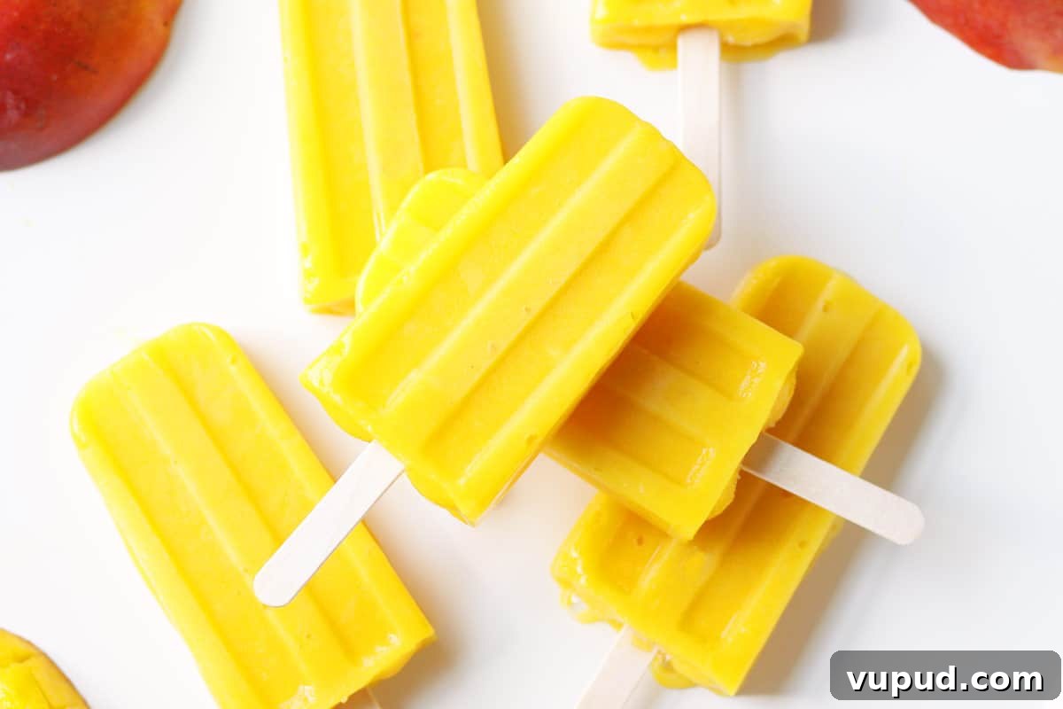 Mango Popsicle Recipe: Creamy, Refreshing Homemade Treat 7 a pile of mango popsicles on a white tray with a sliced fresh mango behind them