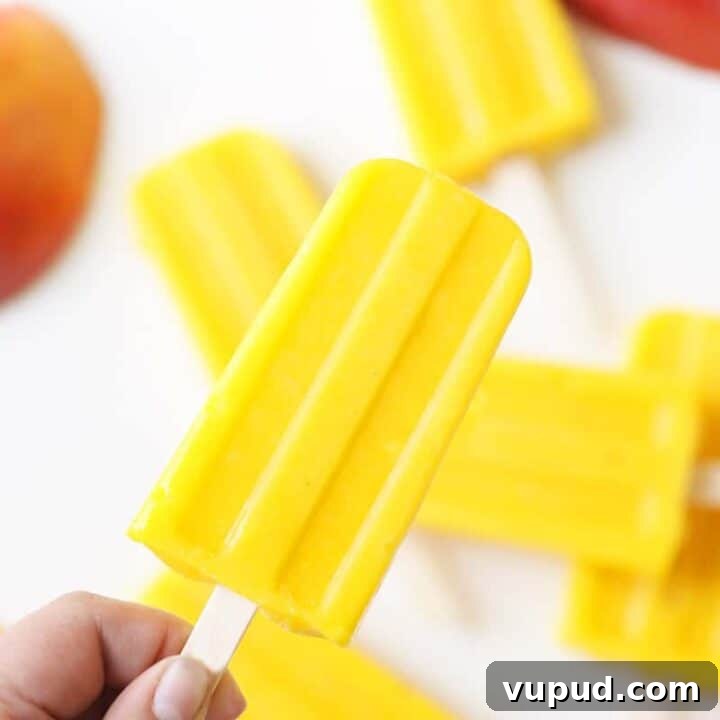 a pile of mango popsicles on a white tray with a sliced fresh mango behind them