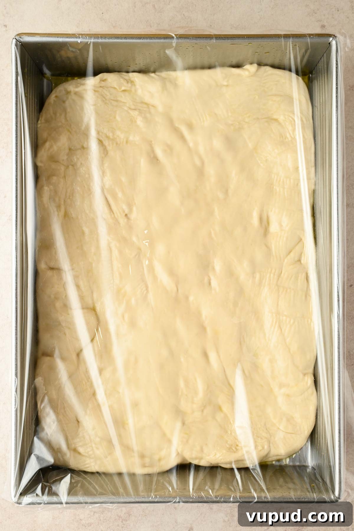 Raspberry Jam Sweet Focaccia Recipe for Soft, Fruity Bread 6 focaccia dough in silver rectangular baking pan covered in plastic wrap.