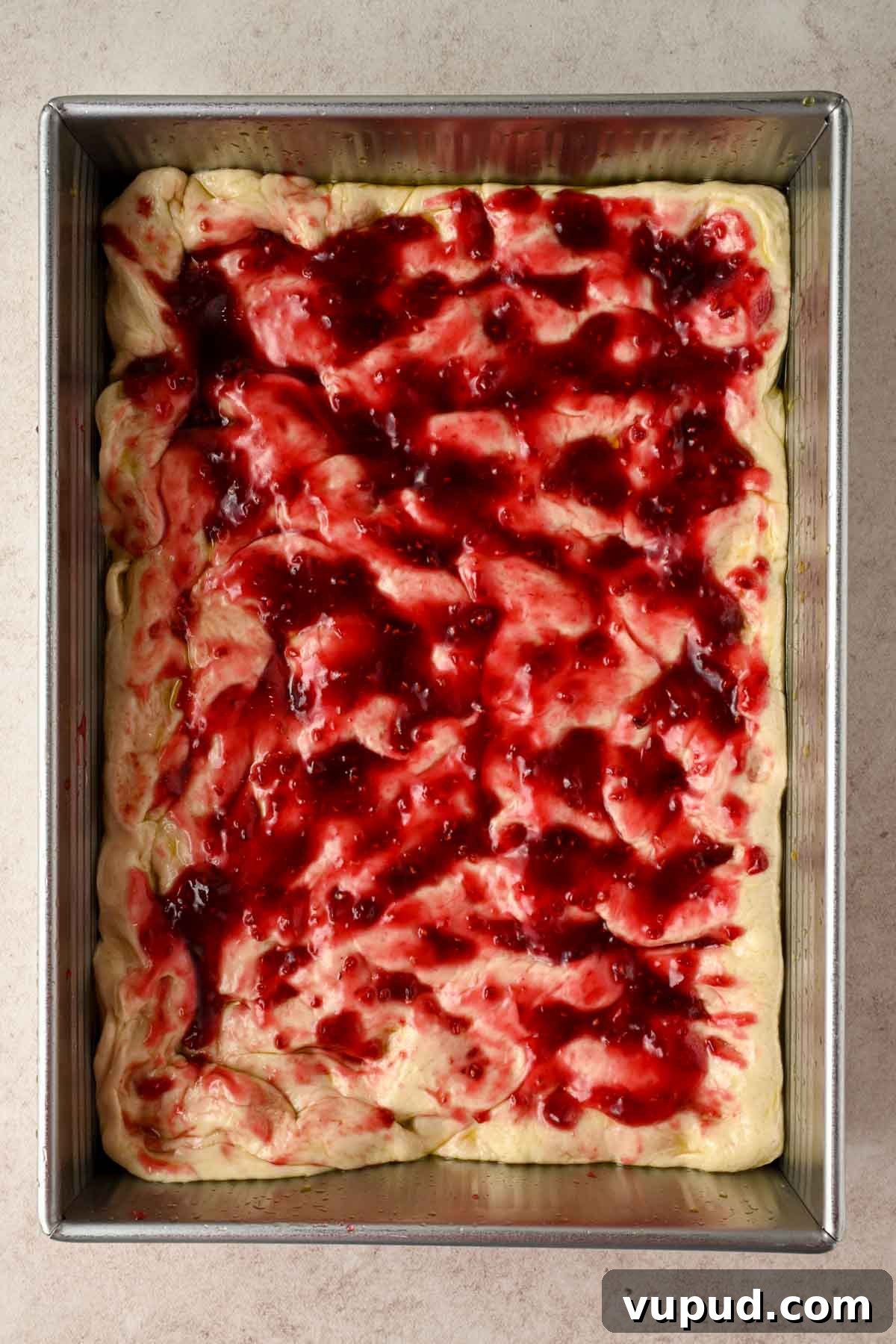 Raspberry Jam Sweet Focaccia Recipe for Soft, Fruity Bread 7 focaccia dough in silver rectangular baking pan spread with raspberry jam.