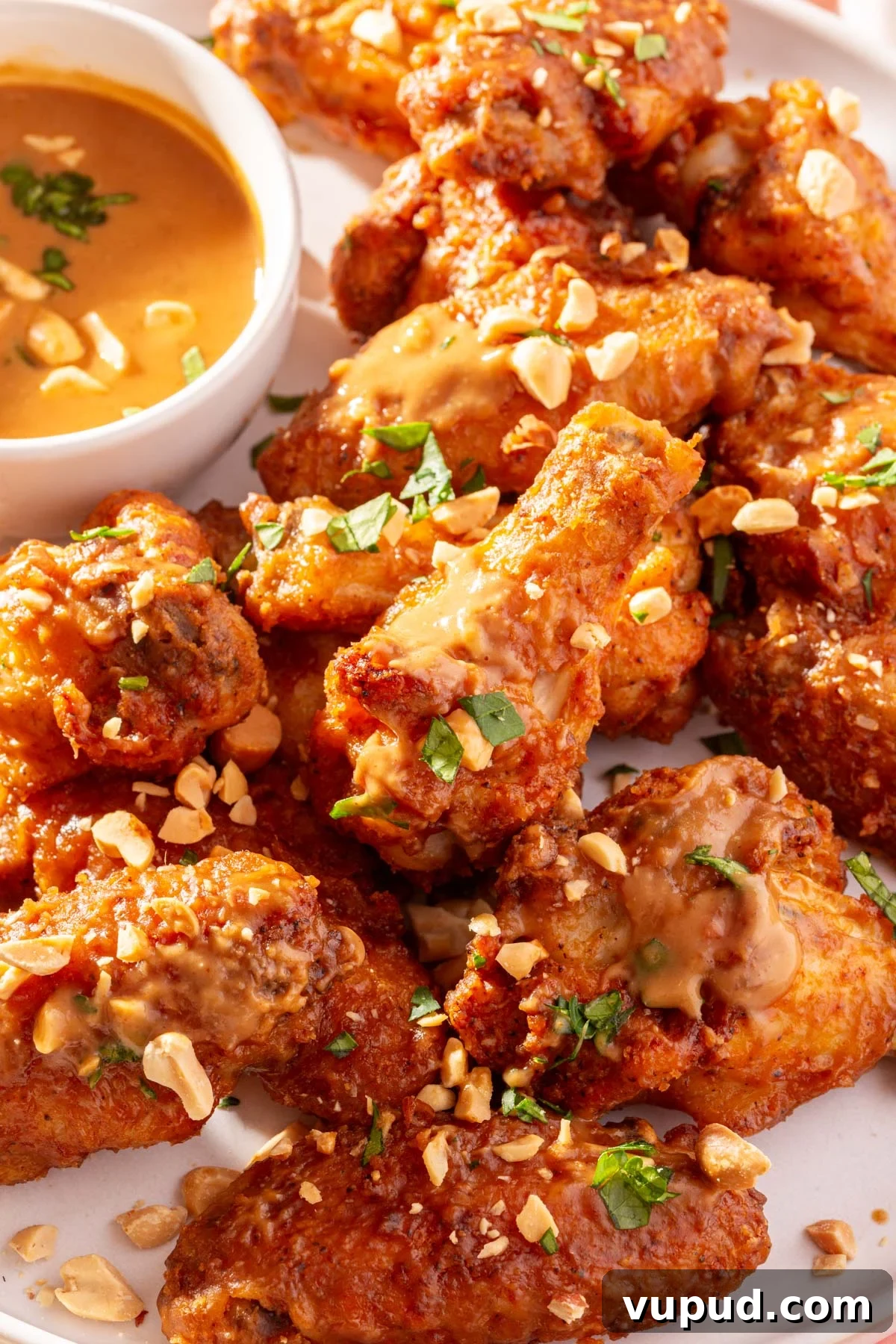 Savory Peanut Butter Glazed Chicken Wings Recipe 2 A close up of a plate of peanut butter chicken wings topped with chopped peanuts and parsley with a side of peanut butter sauce.
