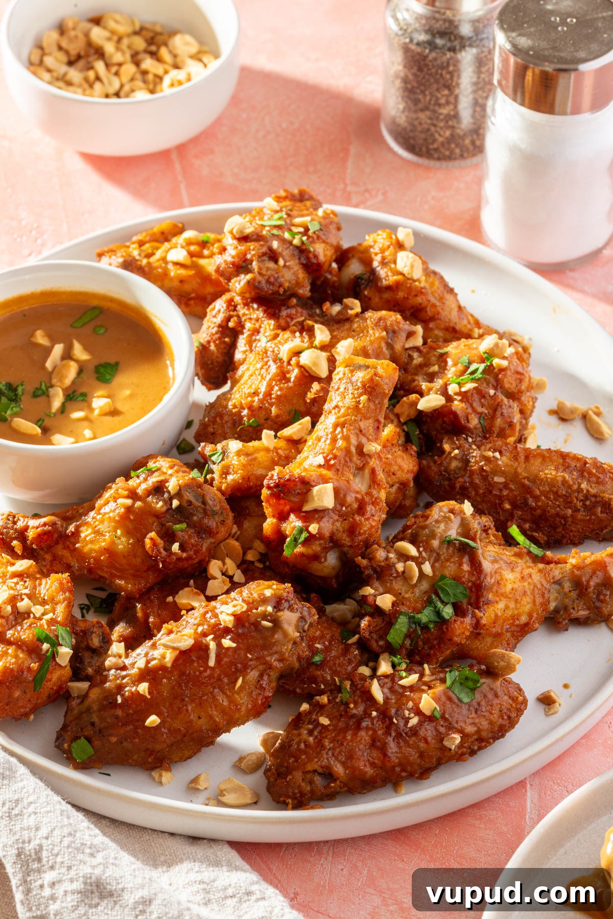 Savory Peanut Butter Glazed Chicken Wings Recipe 4 A plate of peanut butter chicken wings topped with crushed peanuts and parsley with a bowl of peanut butter sauce to the side.