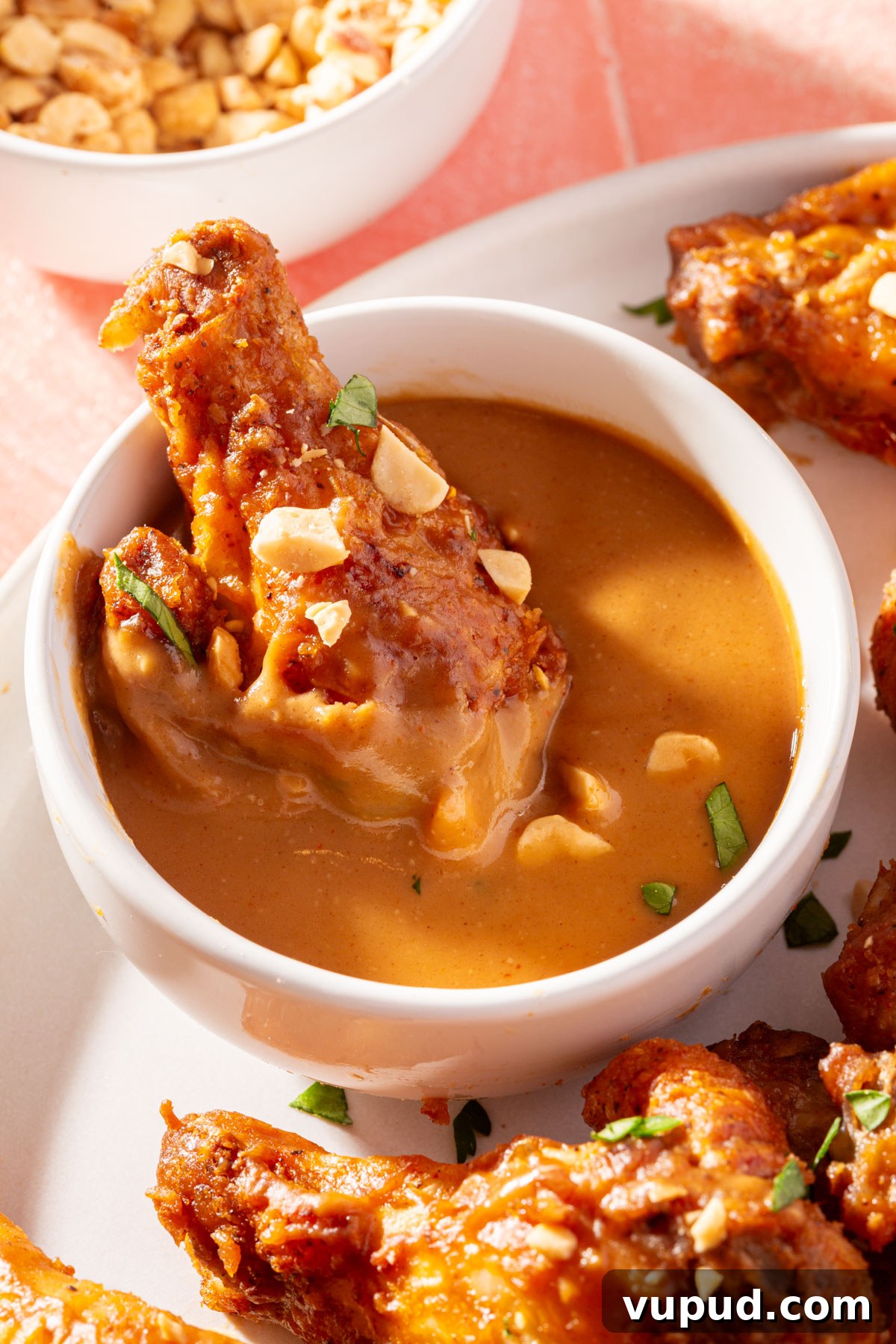 Savory Peanut Butter Glazed Chicken Wings Recipe 5 A peanut butter chicken wing being dipped in a ramekin of peanut butter sauce with a small bowl of chopped peanuts off to the side.