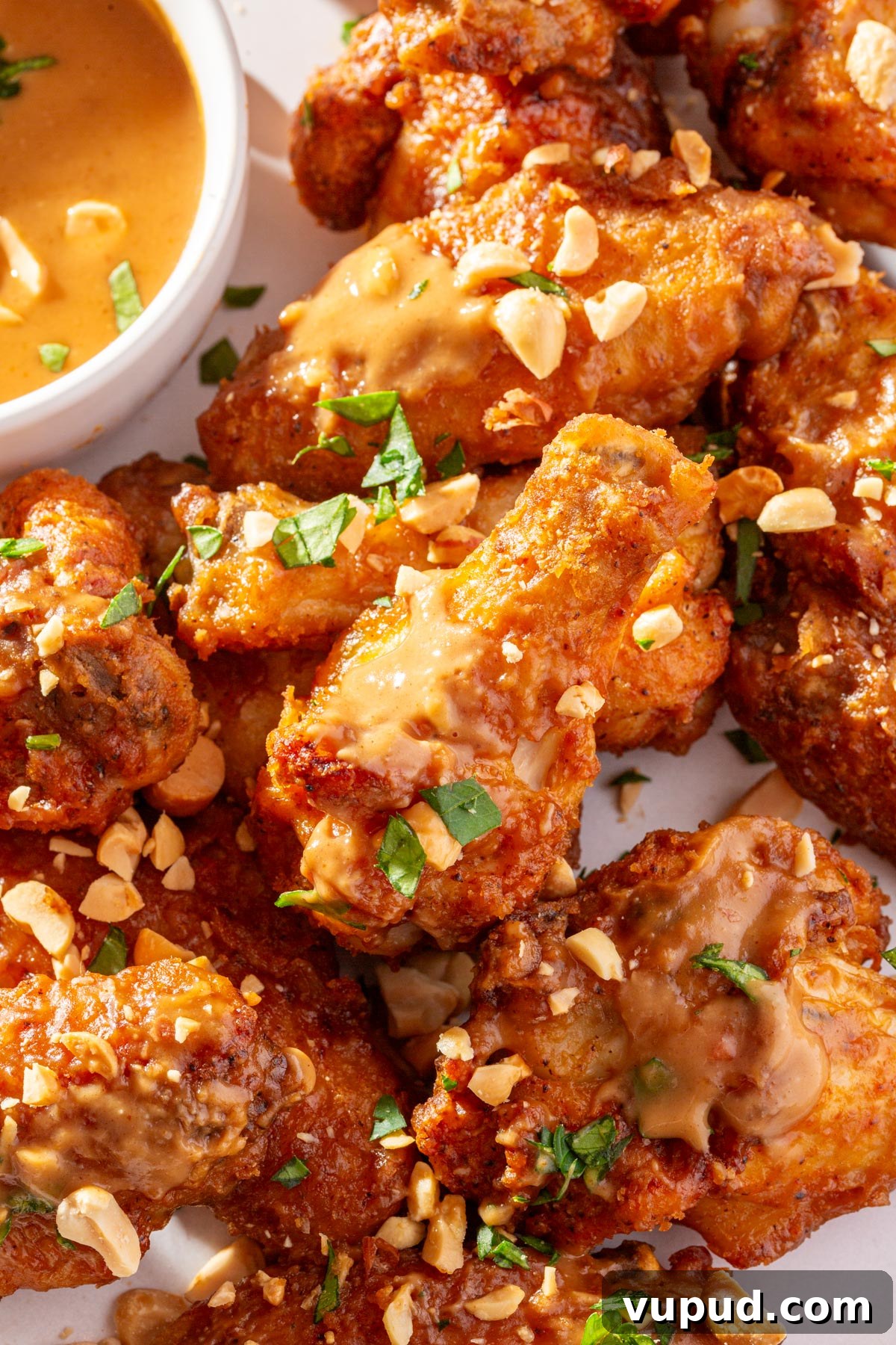 Savory Peanut Butter Glazed Chicken Wings Recipe 6 A close up view of peanut butter chicken wings topped with chopped peanuts on a white plate with a bowl of peanut butter sauce off to the side.