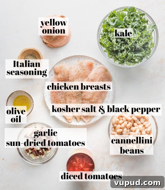 Tuscan Chicken with White Beans and Kale Recipe 3 Labeled overhead photo of thin-sliced chicken breasts seasoned with salt and pepper, cannellini beans, diced tomatoes, minced garlic, sun-dried tomatoes, olive oil, Italian seasoning, yellow onion, and kale, all in prep bowls and ready to cook.