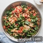 Tuscan Chicken with White Beans and Kale Recipe 8 Skillet full of a Tuscan-inspired chicken dinner with kale, white beans, and sun-dried tomatoes, with salt and pepper in the background for added seasoning.