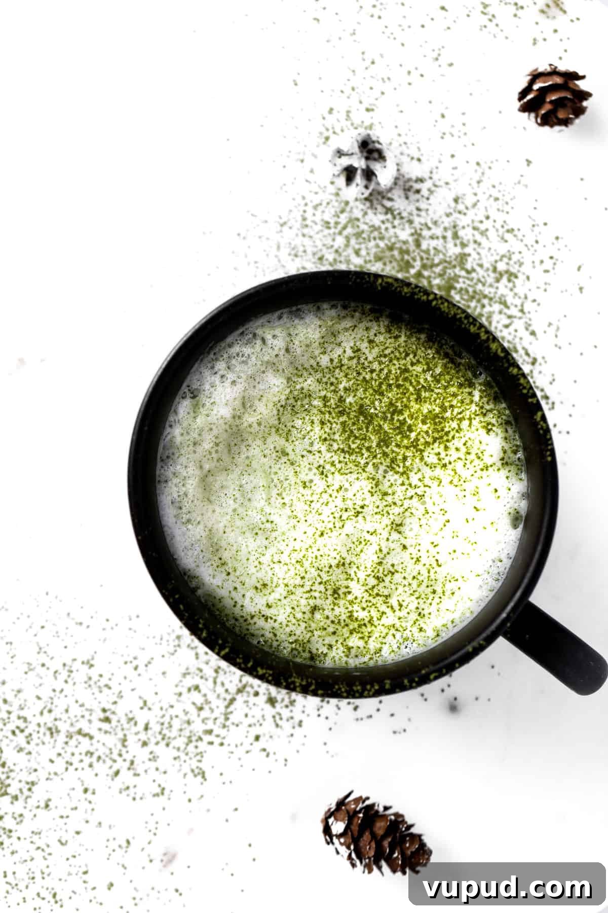 Creamy Oat Milk Matcha Latte Recipe for Perfectly Frothy Mornings 7 A cup of oat milk matcha latte in a black mug, sprinkled with matcha powder on a white table.