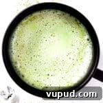 Overhead view of a frothy oat milk matcha latte in a black mug.