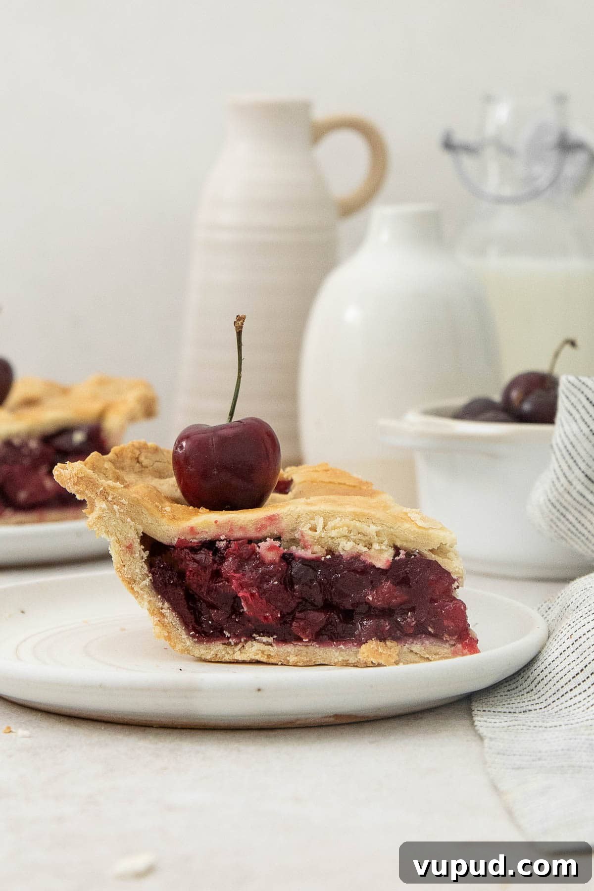 Gluten-Free Cherry Pie Recipe with Flaky Homemade Crust 3 a slice of cherry pie with a cherry on top on a white plate.
