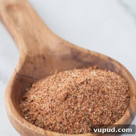 Large wooden spoon filled with brownish red cajun spice seasoning sitting on a marble table