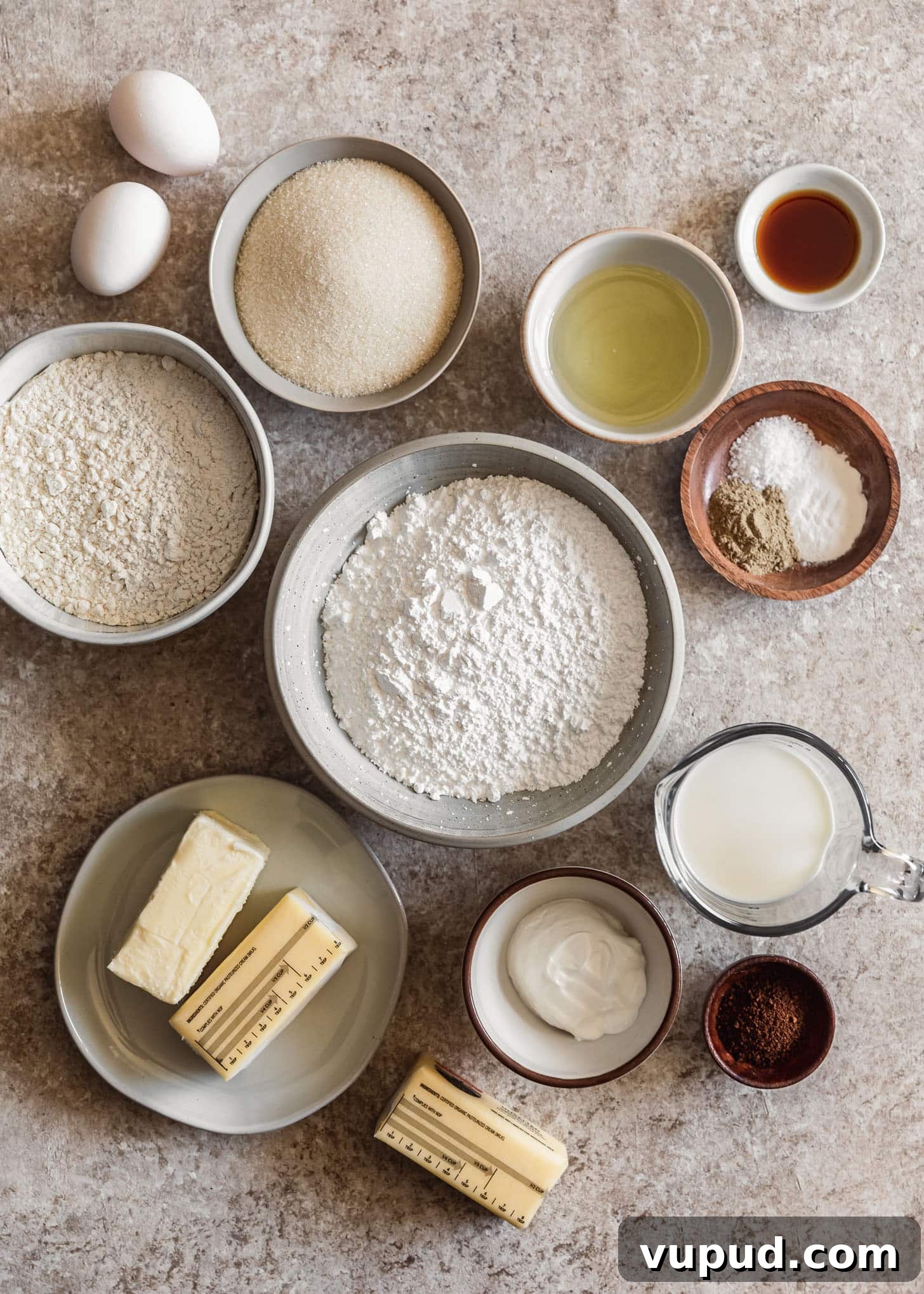 Cardamom Cake with Silky Coffee Buttercream 3 White and wood bowls of baking ingredients like flour, sugar, butter, spices, milk, vanilla, and sour cream on a beige counter.