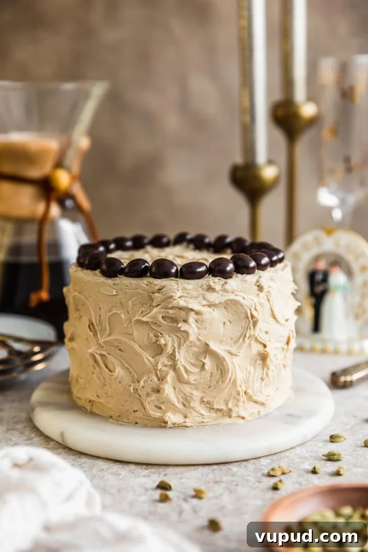 Cardamom Cake with Silky Coffee Buttercream 8 Cardamom cake with coffee buttercream on a marble plate next to a wood bowl of cardamom pods, white linen, Chemex, and wedding cake topper on a beige background.