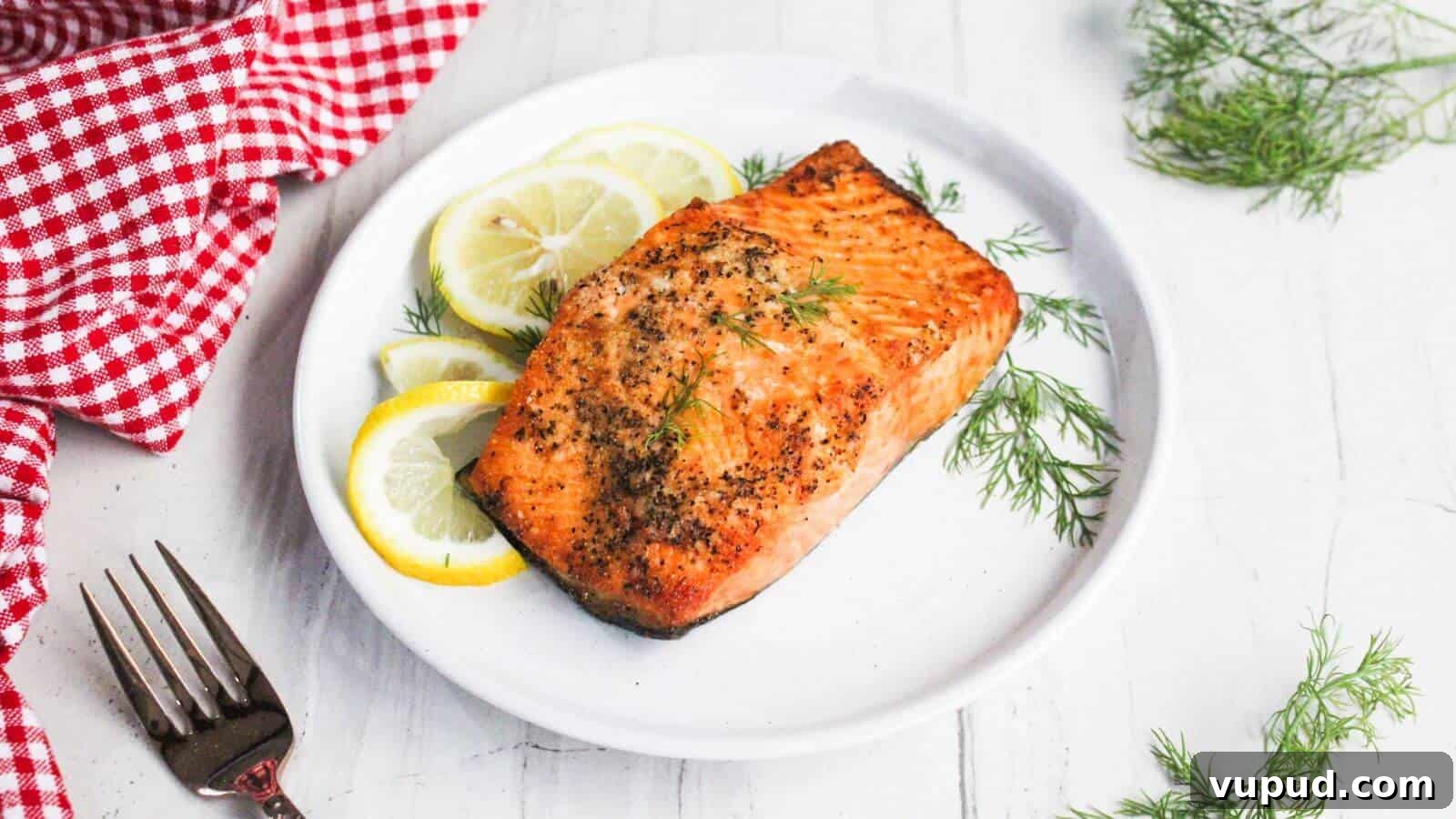 30 Flavorful Low-Carb Main Dishes That Feel Like Real Meals 24 Grilled salmon fillet on a white plate garnished with lemon slices and dill, next to a red checkered cloth and a fork.