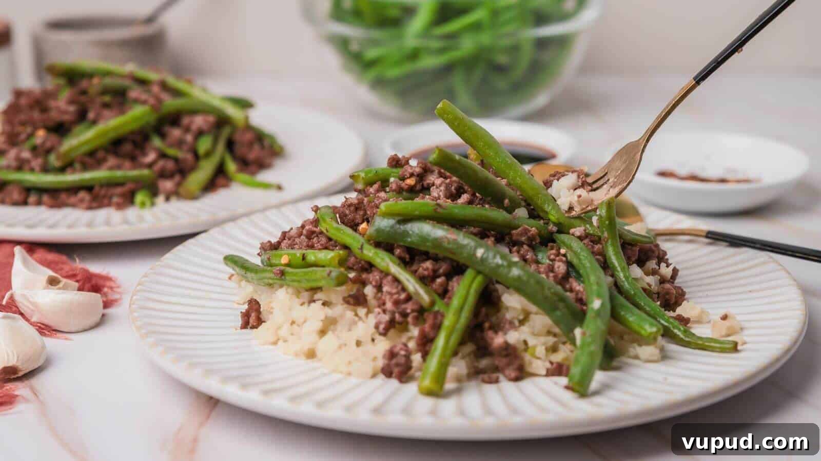 30 Flavorful Low-Carb Main Dishes That Feel Like Real Meals 25 Plate with ground beef, green beans, and cauliflower rice. Fork on the plate, garlic cloves nearby, and a bowl of green beans in the background.