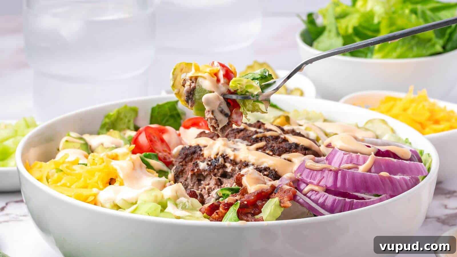 30 Flavorful Low-Carb Main Dishes That Feel Like Real Meals 28 A bowl of salad with sliced red onions, lettuce, tomatoes, shredded cheese, ground beef, bacon, and dressing; a fork holds a bite above the bowl.