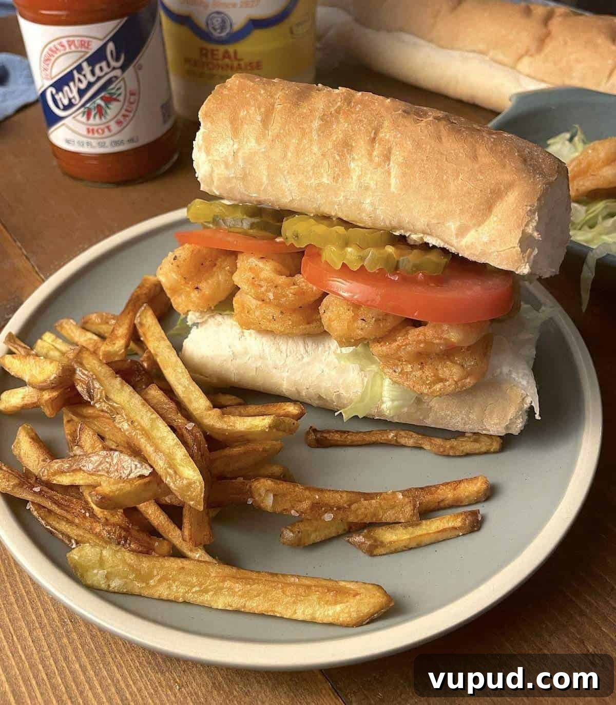Crispy Fried Shrimp Po' Boy Sandwich Recipe 2 A fully dressed fried shrimp po boy on a blue plate with french fries.