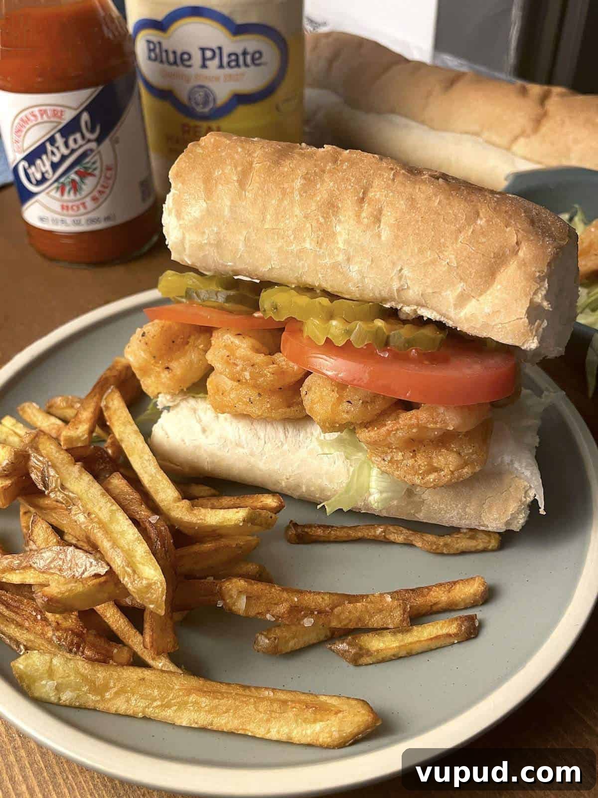 Crispy Fried Shrimp Po' Boy Sandwich Recipe 10 A fully dressed fried shrimp po boy on a blue plate with a jar of mayonnaise and hot sauce.