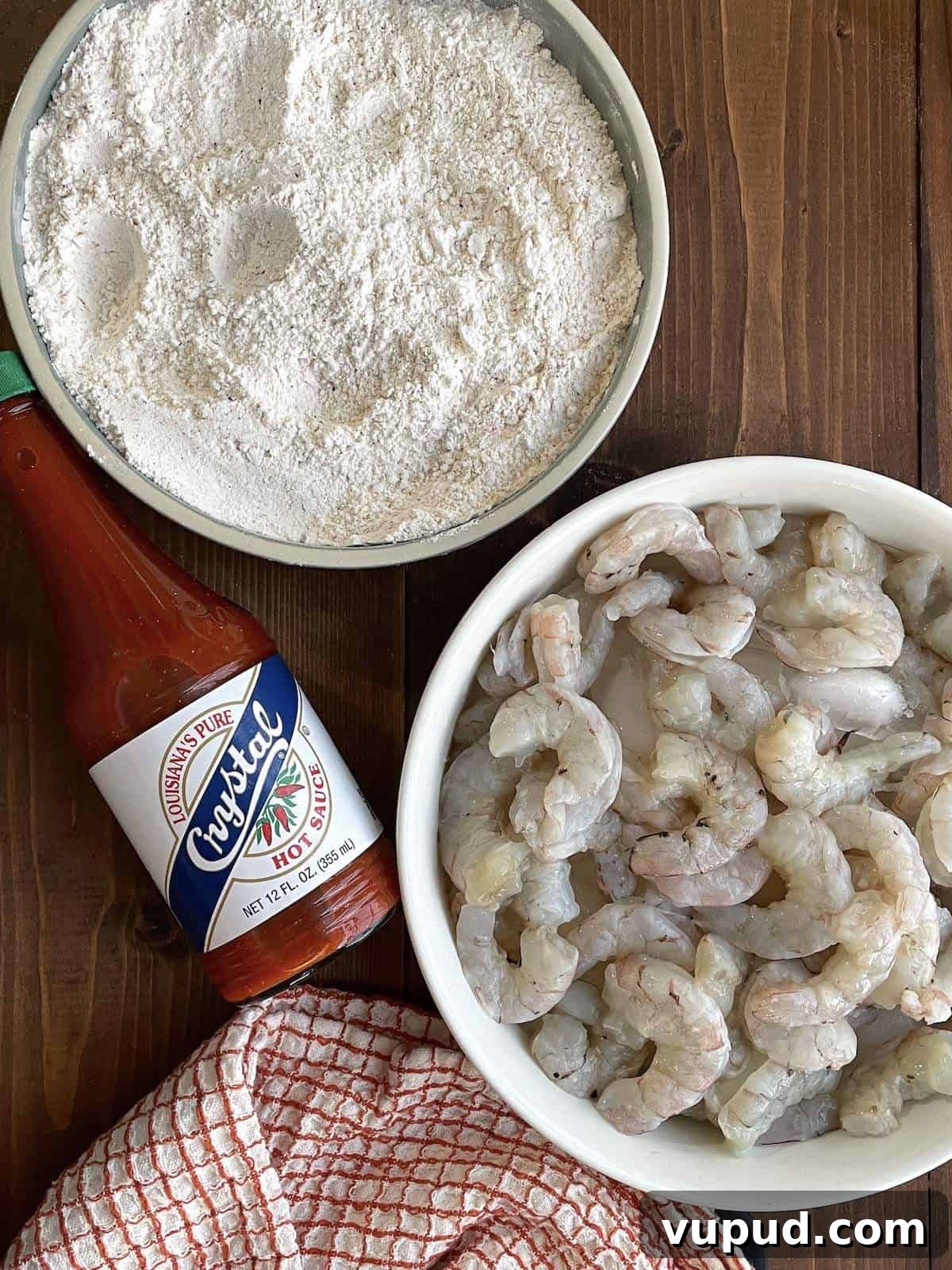Crispy Fried Shrimp Po' Boy Sandwich Recipe 6 A bowl of shrimp and a bowl of seasoned flour with a bottle of hot sauce.