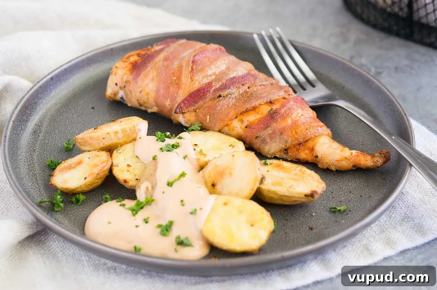 Crispy Bacon-Wrapped Chicken Breasts with Garlic Herb Glaze 3 close up image of chicken wrapped in bacon with roasted potatoes on a plate