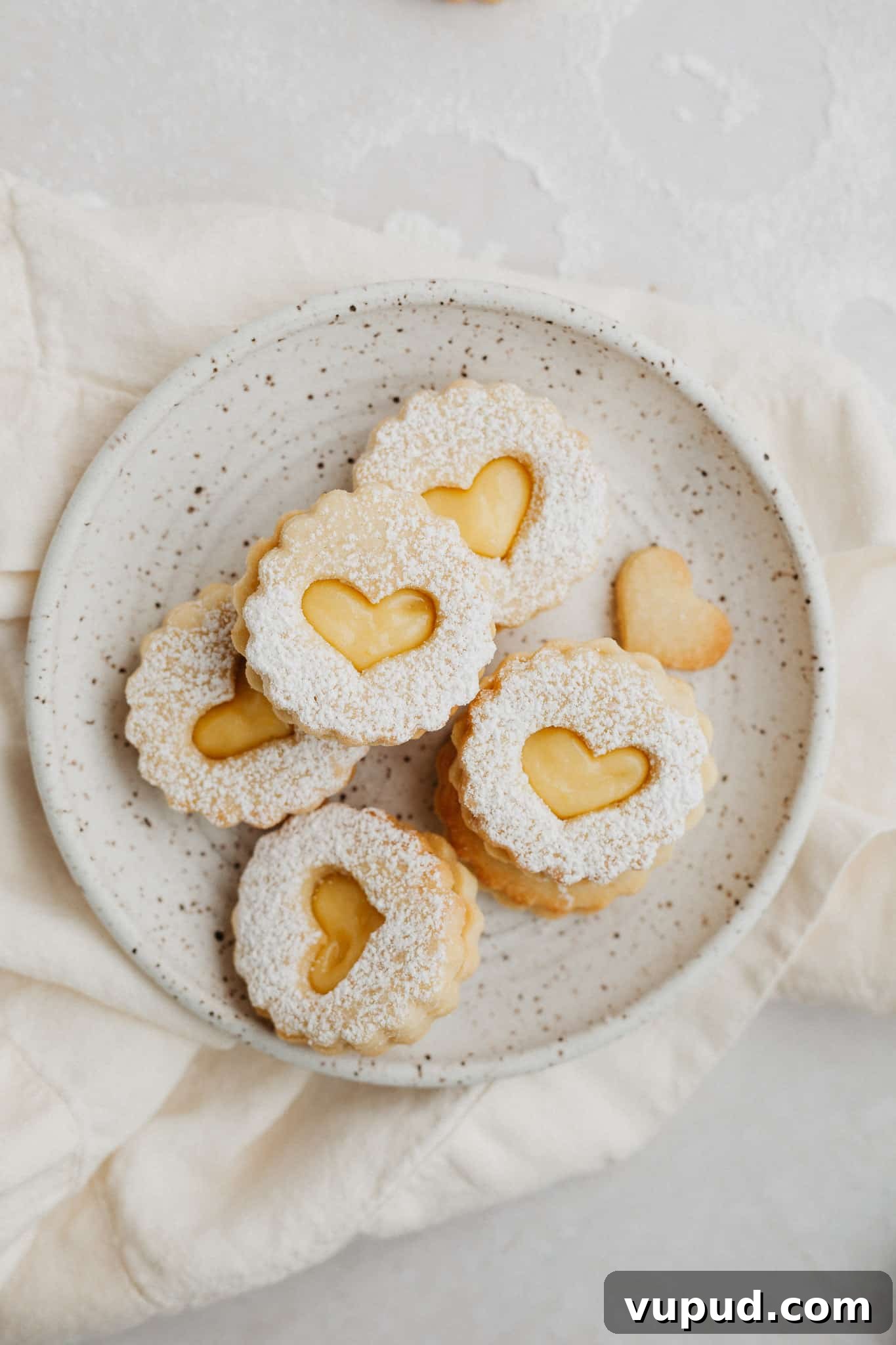 Zesty Lemon Curd Thumbprint Cookies 2 a small speckled beige plate with heart shaped lemon curd cookies dusted with confectioners' sugar.