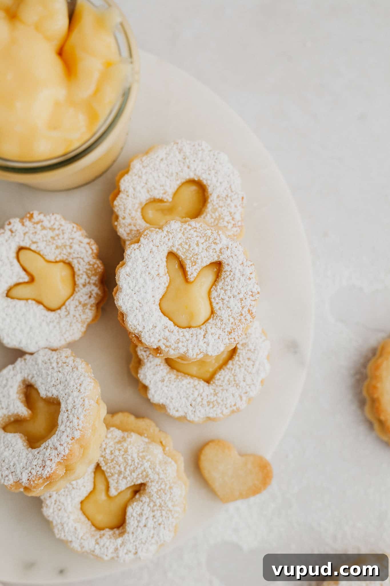 Zesty Lemon Curd Thumbprint Cookies 8 lemon curd cookies with rabbit shaped cutouts on a marble surface.