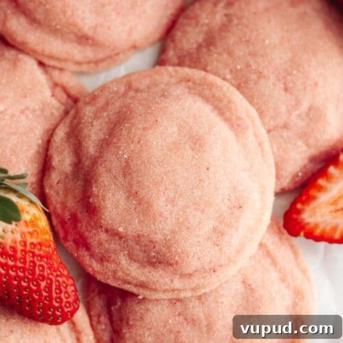 A close up of pink strawberry sugar cookies on parchment paper, there are a few sliced strawberries.