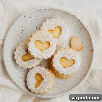 Zesty Lemon Curd Thumbprint Cookies 13 a small speckled beige plate with heart shaped lemon curd cookies dusted with confectioners' sugar.