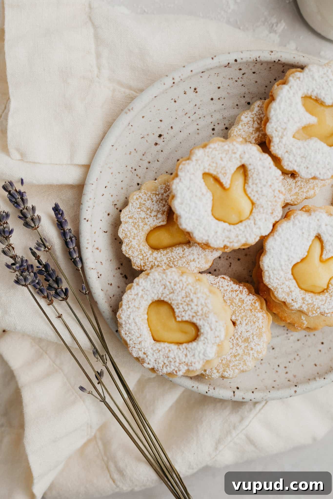 Zesty Lemon Curd Thumbprint Cookies 7 a small speckled beige plate with heart shaped lemon curd cookies dusted with confectioners' sugar.
