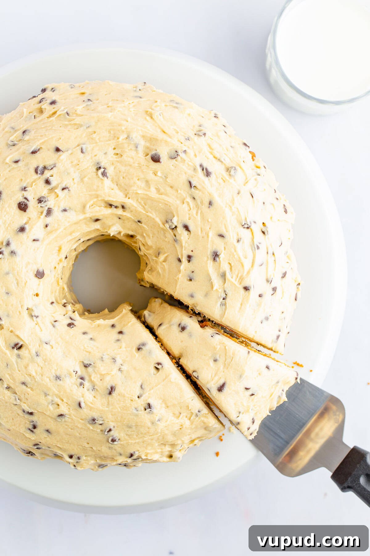 Chocolate Chip Bundt Cake with Cookie Dough Glaze Overhead image of chocolate chip bundt cake with cake server taking a slice out, on white cake stand