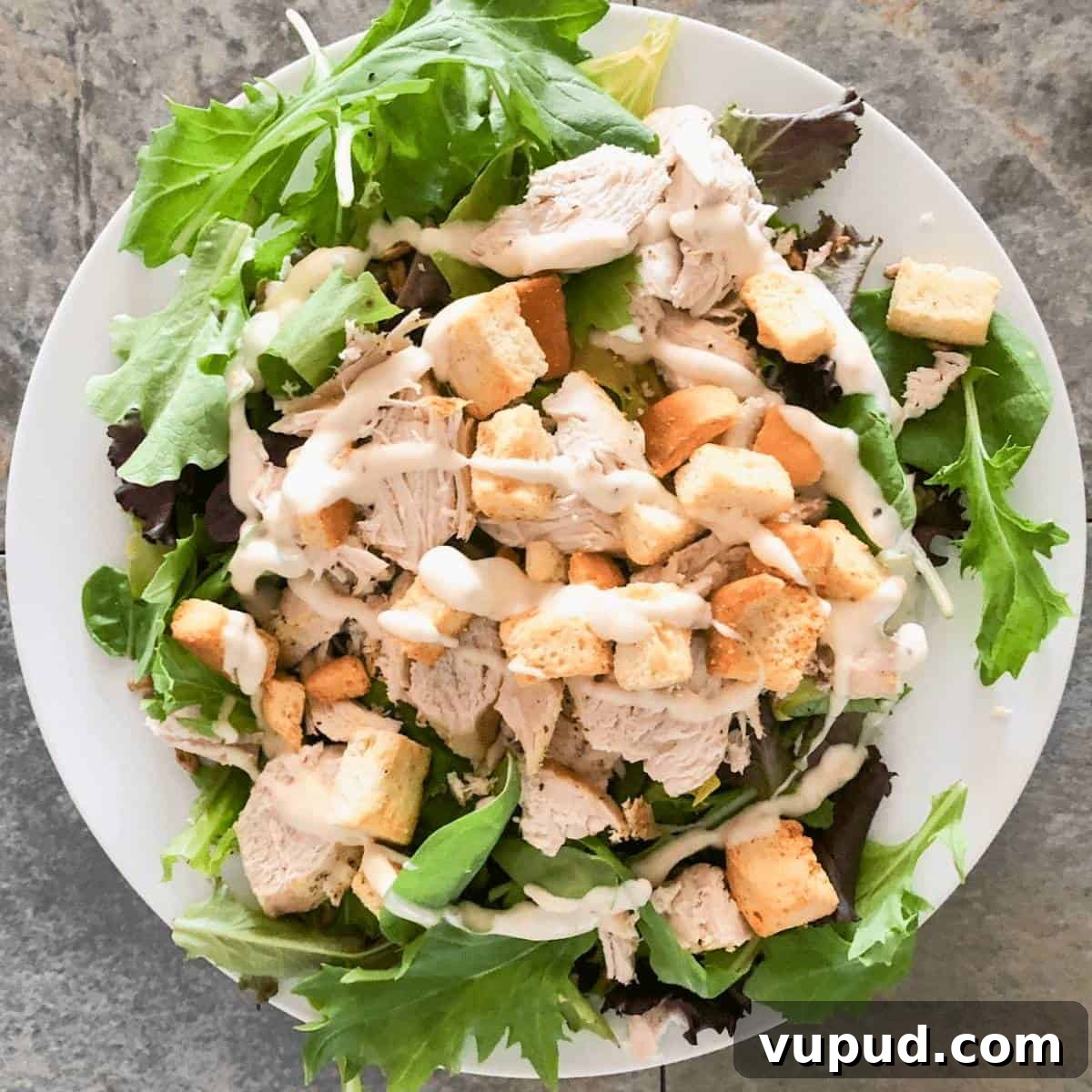 Shredded chicken breasts on a green salad, topped with ranch dressing.