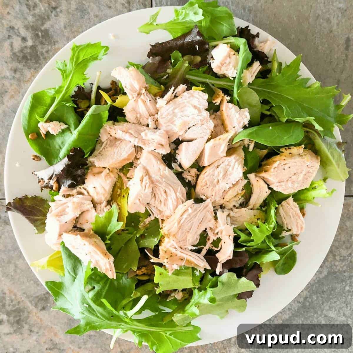 Shredded cooked chicken breasts on a green salad for a quick dinner.