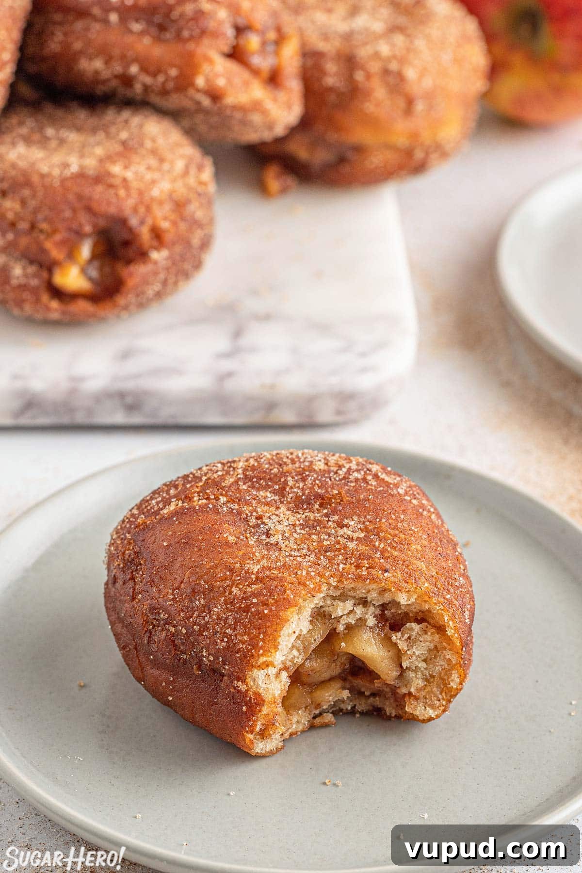Caramel Apple Donut Recipe: Homemade Baked Apple Donuts with Streusel 11 Apple Donut on a gray plate with a bite taken out of it, with more donuts in the background.