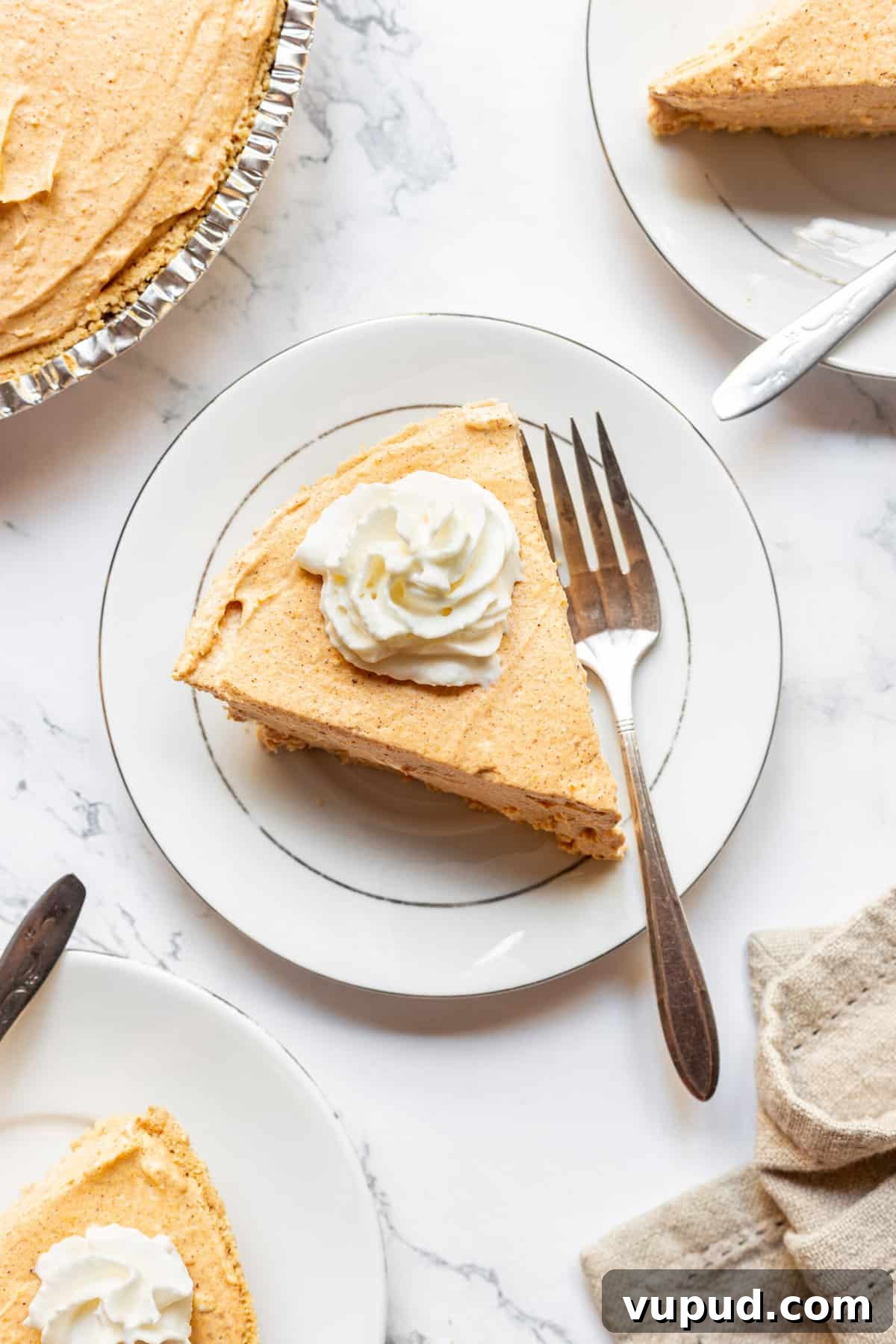 No-Bake Pumpkin Cheesecake with Gingersnap Crust 3 top down image of a slice of pumpkin cheesecake served on a white round plate with a silver fork