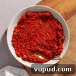 A close-up shot of sun-dried tomato spread in a small bowl on a cutting board.