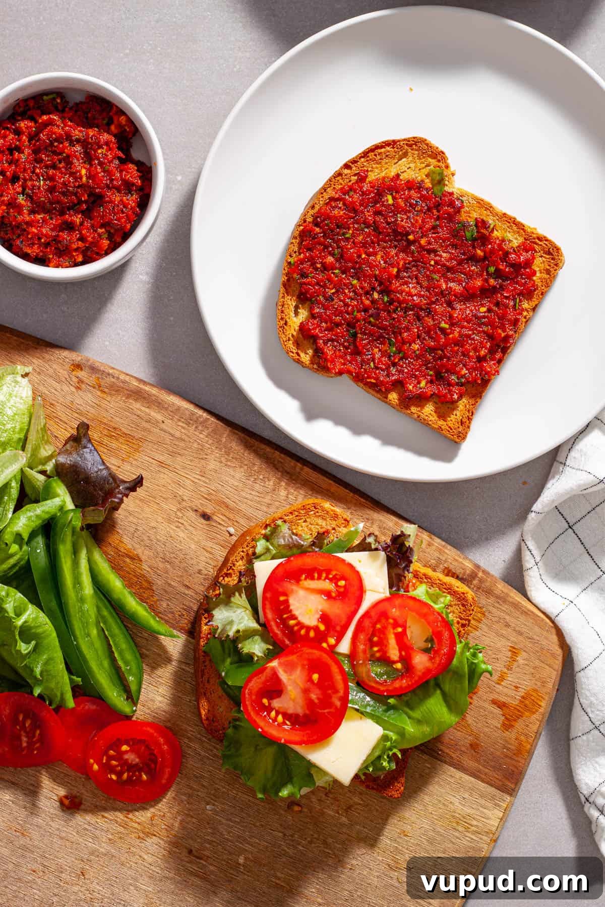 A sandwich with vegetables, cheese and homemade sun-dried tomatoes getting assembled on a cutting board.