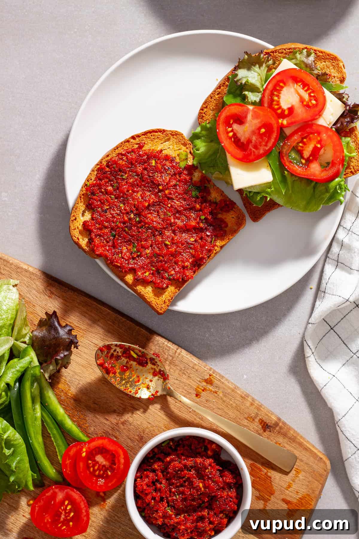 A plate with a sandwich made with homemade sun-dried tomato spread, with lettuce, tomato, peppers and cheese.