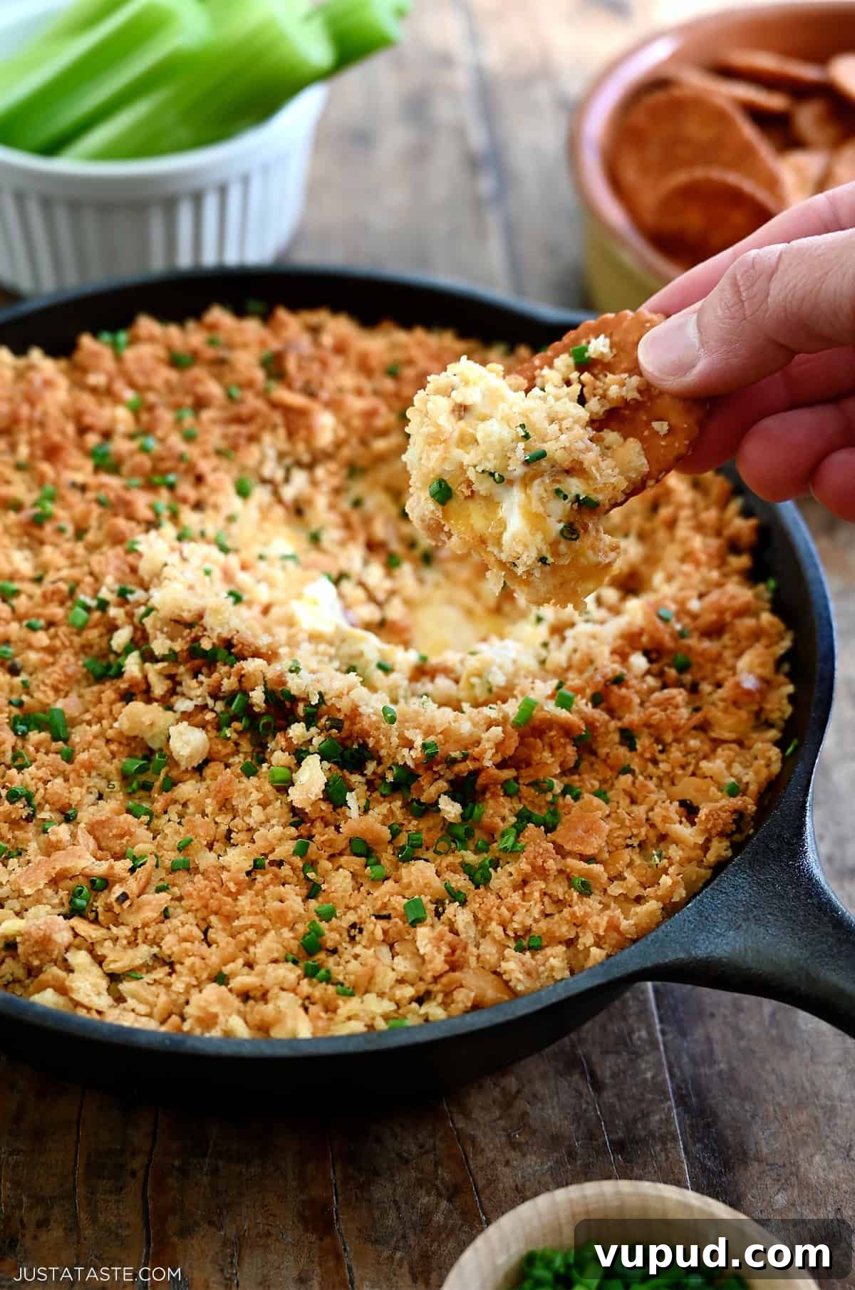 Creamy Jalapeño Popper Dip Recipe for Parties and Game Day 12 A hand holding a Ritz cracker dips it into a cheesy jalapeño popper dip in a cast iron skillet.