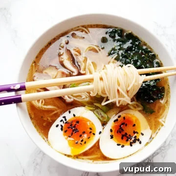 a bowl of vegetarian miso ramen with kale, mushrooms and boiled egg with chopsticks resting on it