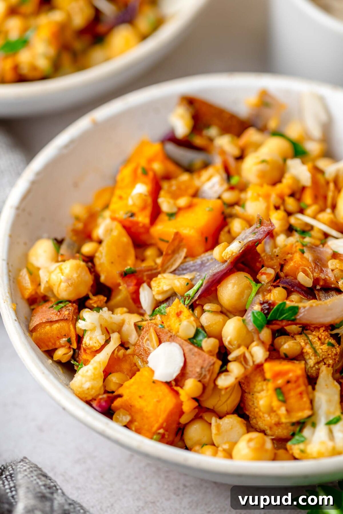 Close-up of a bowl with roasted sweet potato, cauliflower, chickpeas, lentils and chopped herbs.