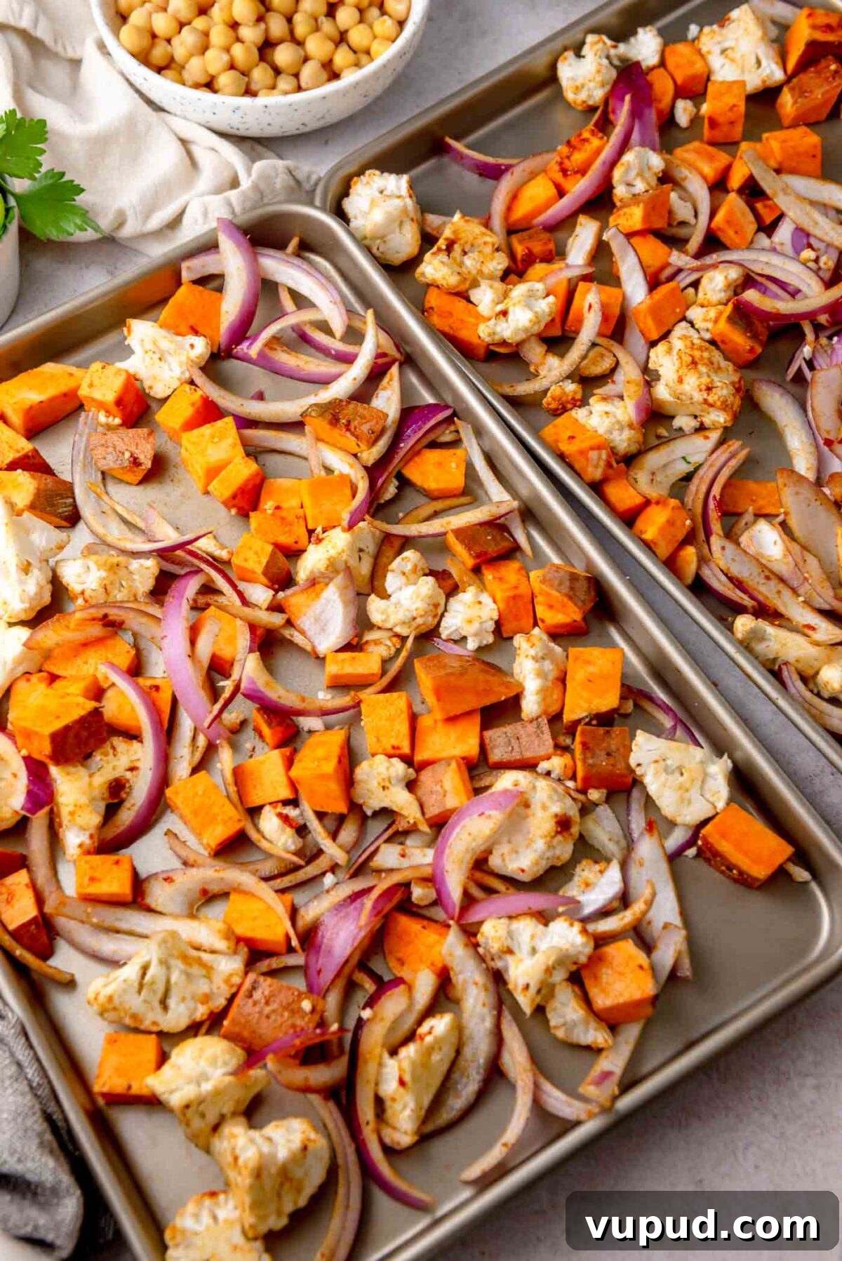 Cauliflower, sweet potato and red onion spread on a baking sheet before roasting.
