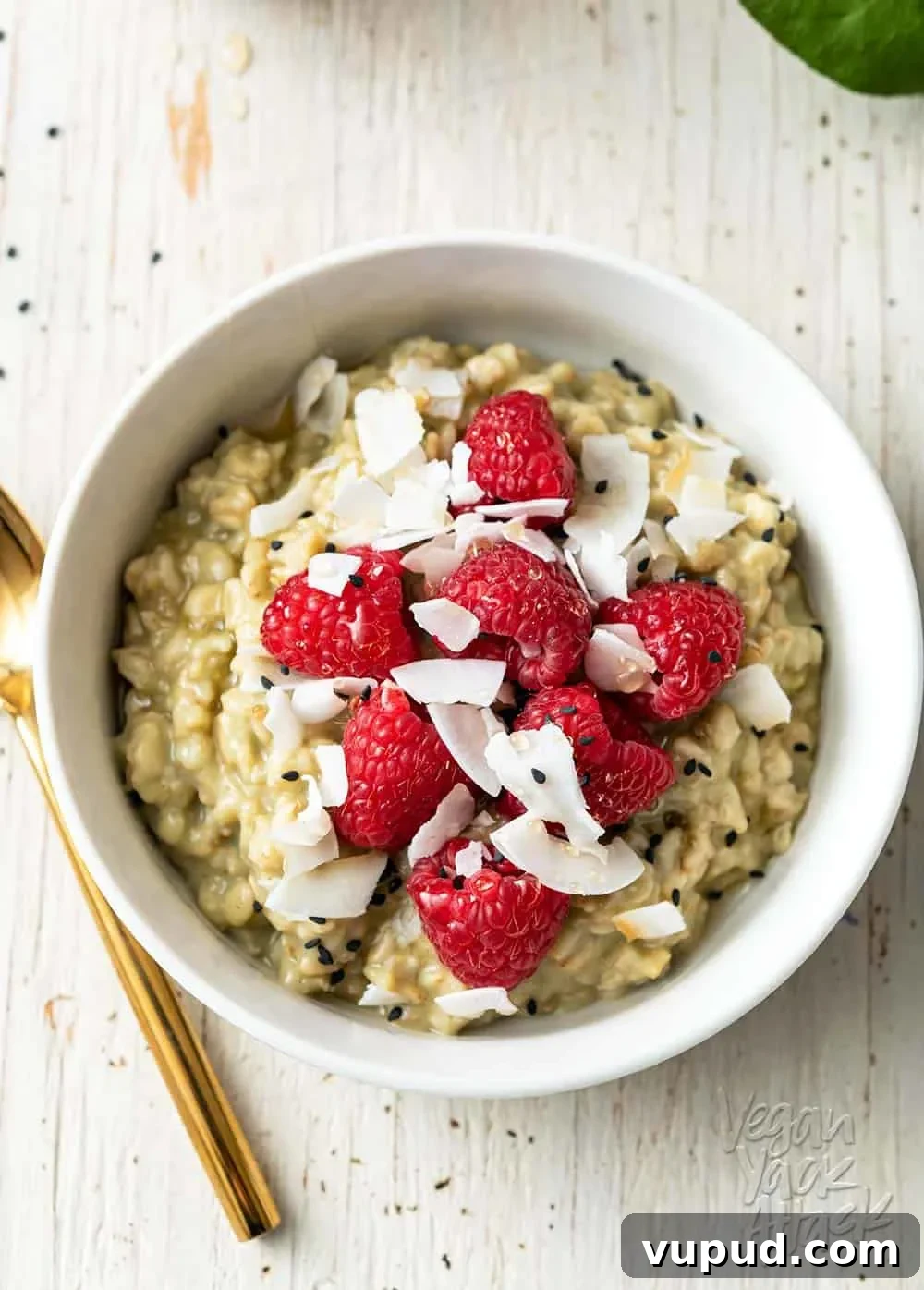 Matcha Oatmeal Meal Prep: Plant-Based Breakfast for Busy Mornings 7 Image of white bowl with matcha oatmeal, topped with raspberries, on a white wood background