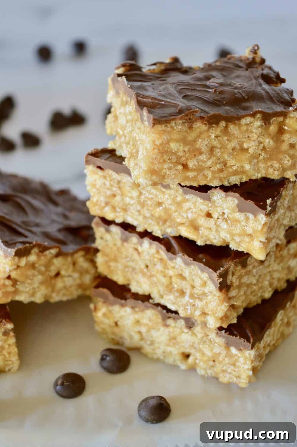 Caramel Peanut Butter Krispie Bars Without Marshmallows 4 Caramel Peanut Butter Rice Krispie Treats stacked up high on a white top with chocolate chips in the background.