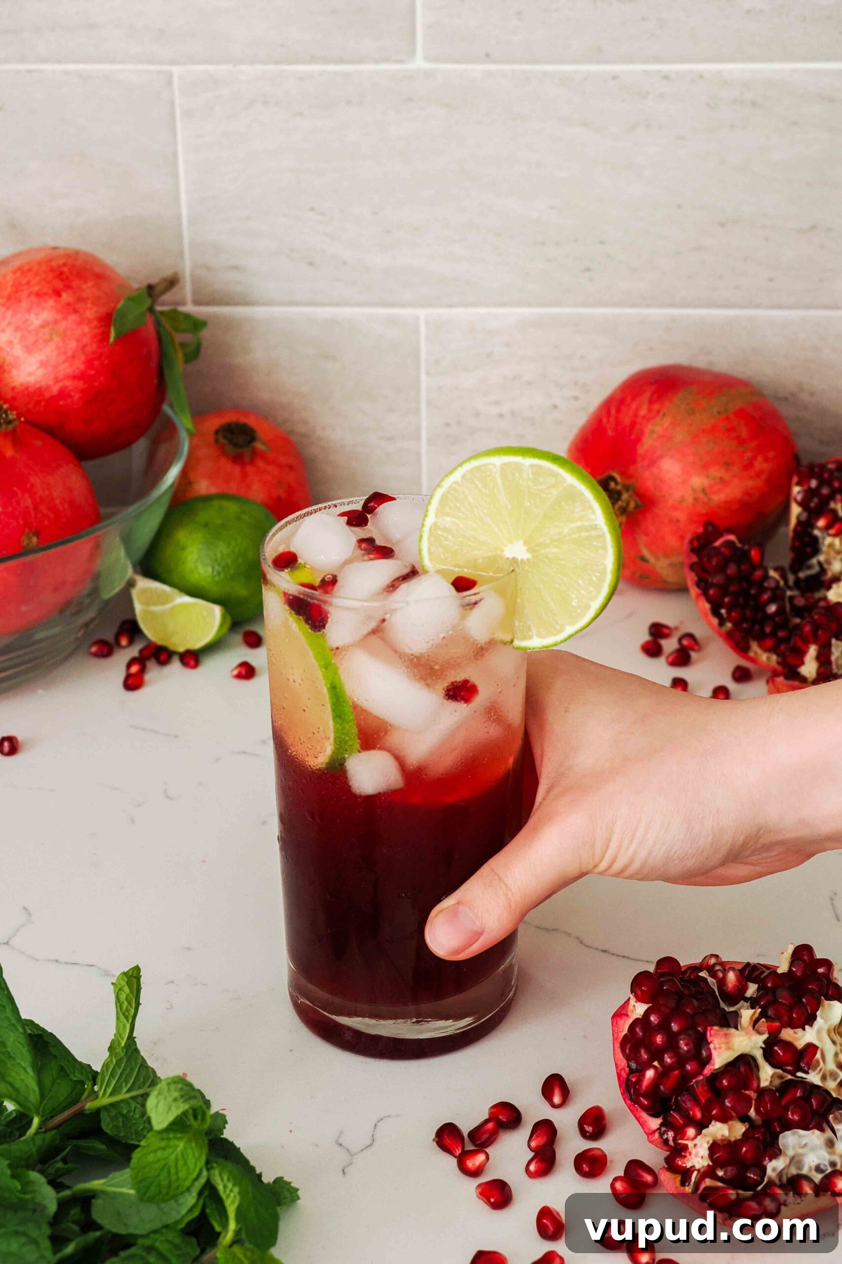 Pomegranate Mojito Recipe: Refreshing Sparkling Cocktail Guide 2 A hand holds a pomegranate mojito in a tall glass.